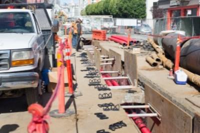 Utility trench with equipment and safety barriers on 4th Street construction site.