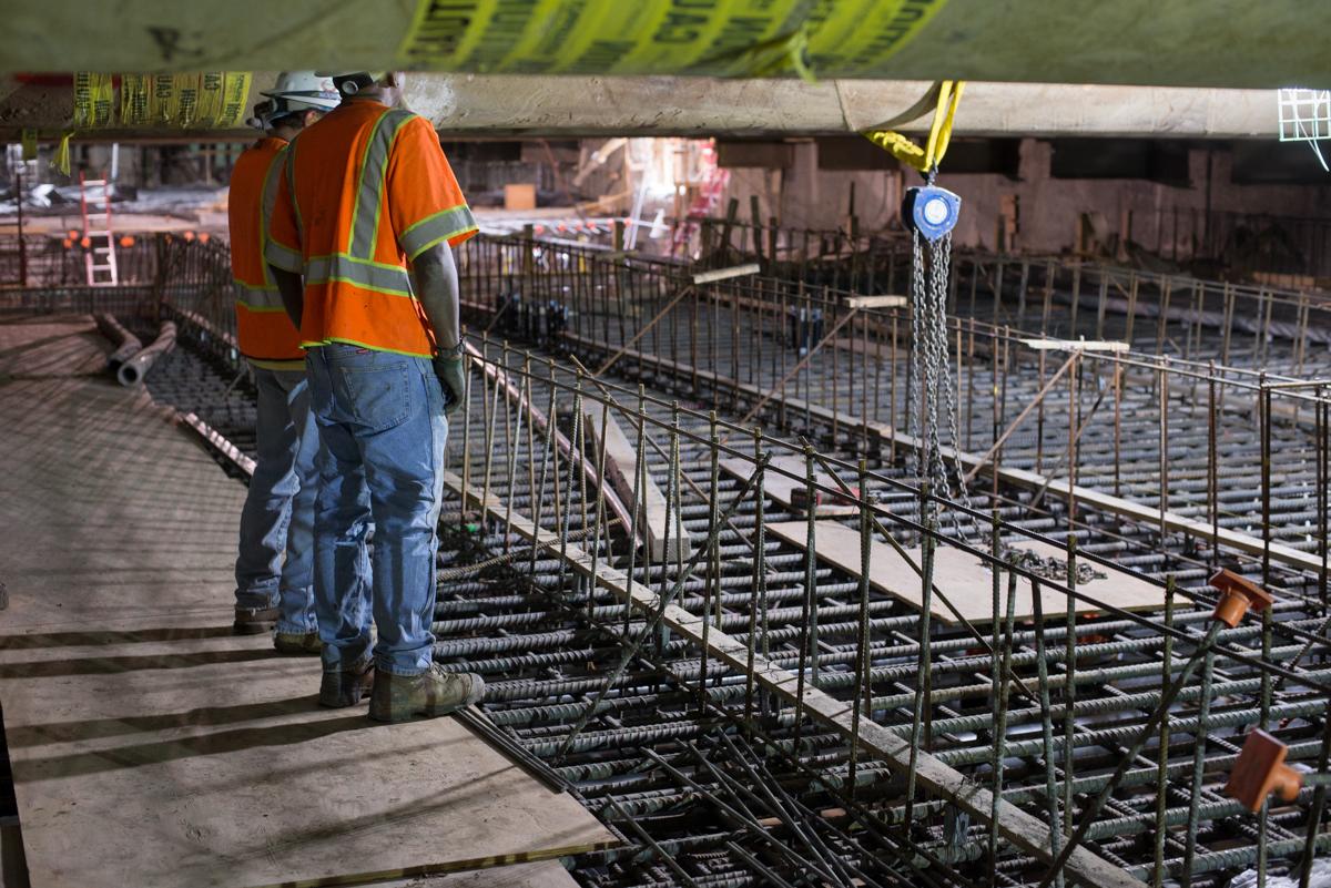 Construction worker in safety vest inspecting steel rebar framework at station platform level.