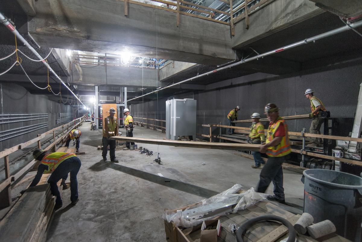 Workers in safety vests construct concrete forms inside an underground transit station platform.