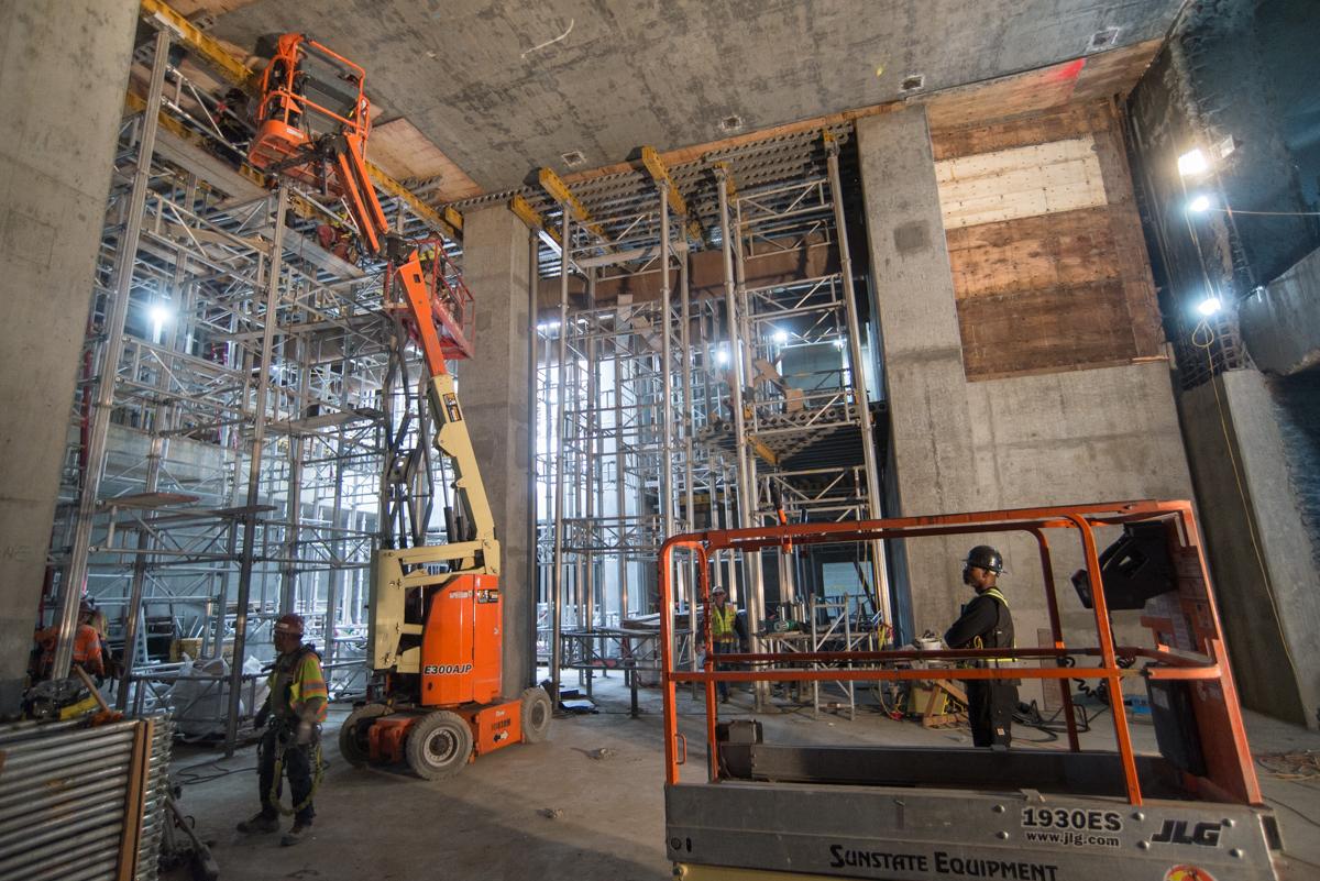 Construction workers operate lift equipment inside an underground transit station headhouse under development.