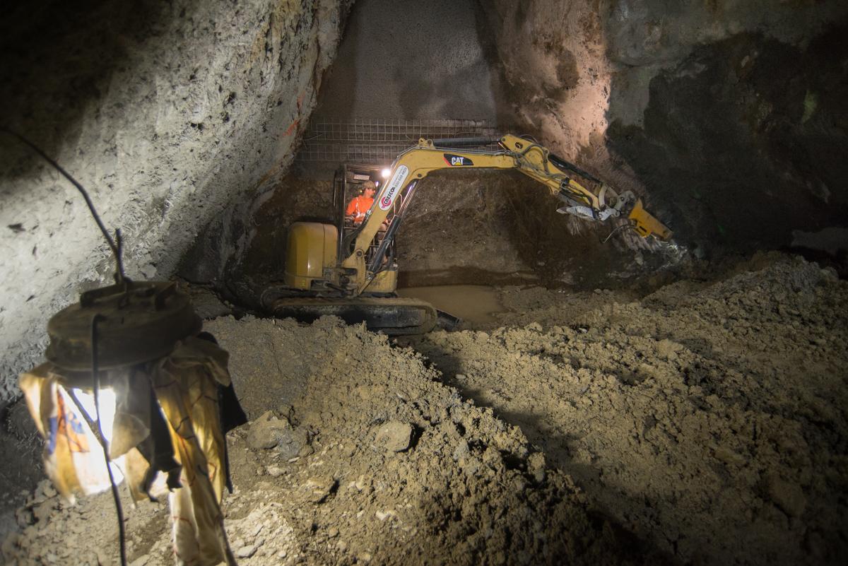 Excavator removing concrete in underground tunnel to expose rebar for future floor slab connection.