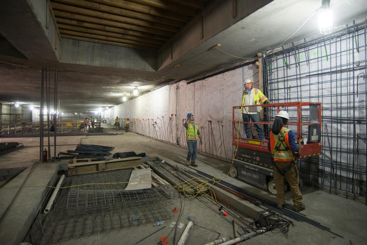 Construction workers in safety gear operate equipment inside an underground transit station under construction.