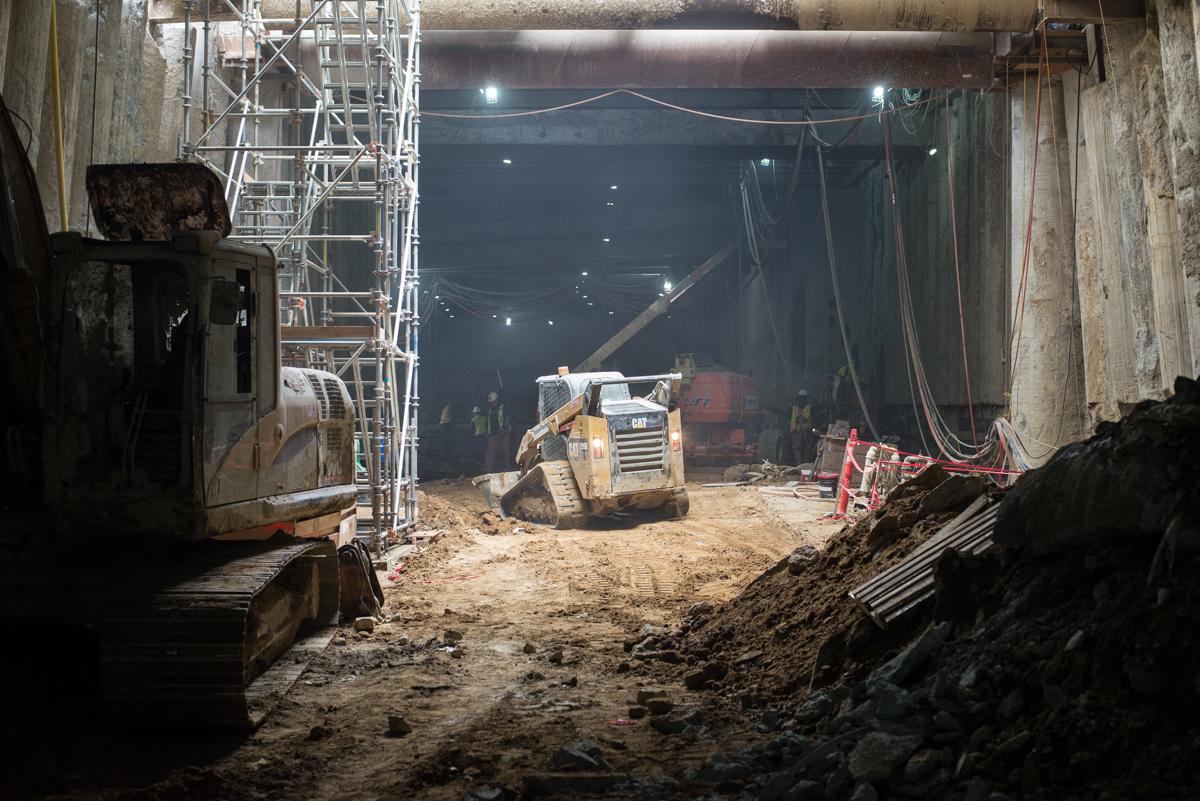 Construction equipment moves soil inside underground station box during transit tunnel renovation work.