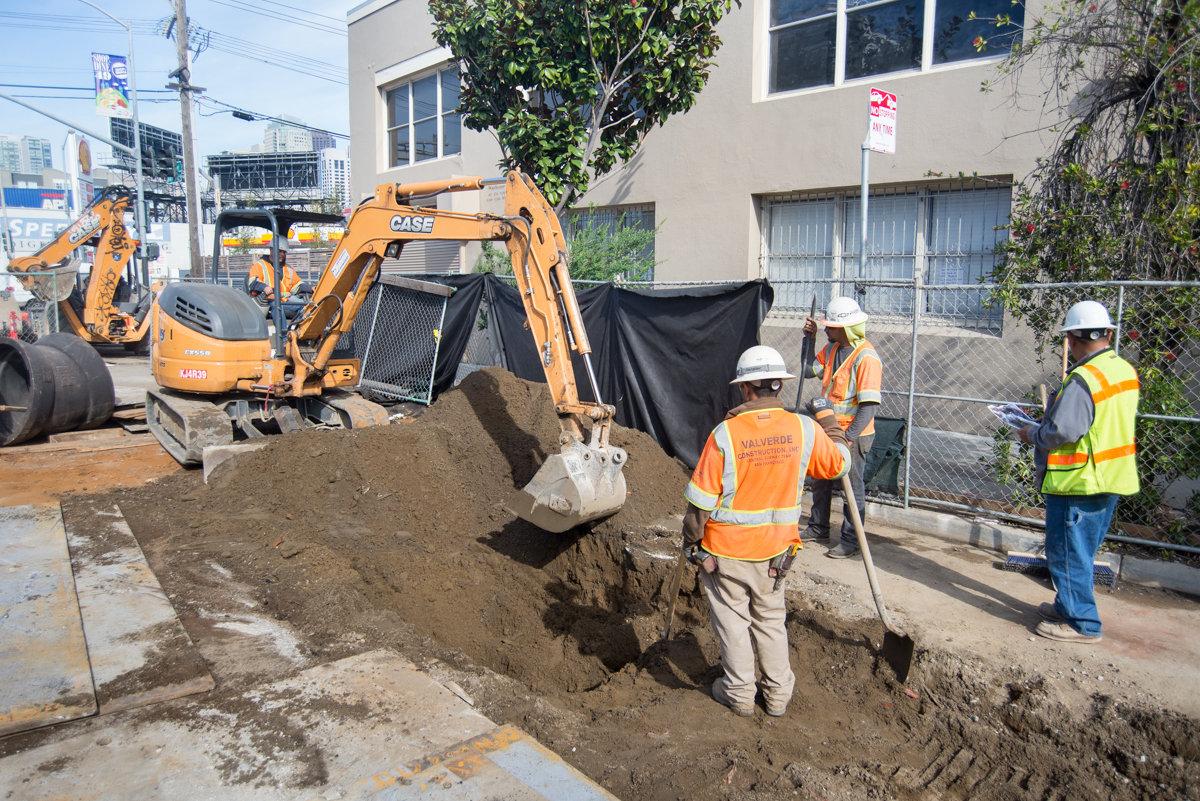 Construction workers operate excavator to remove pavement for trench work on 4th Street.