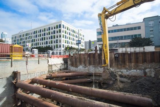 Construction excavation at Yerba Buena Moscone Station with long-reach excavator removing materials from underground headhouse.