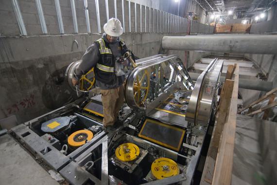 Worker in hard hat and safety vest installing elevator machinery in underground transit station.
