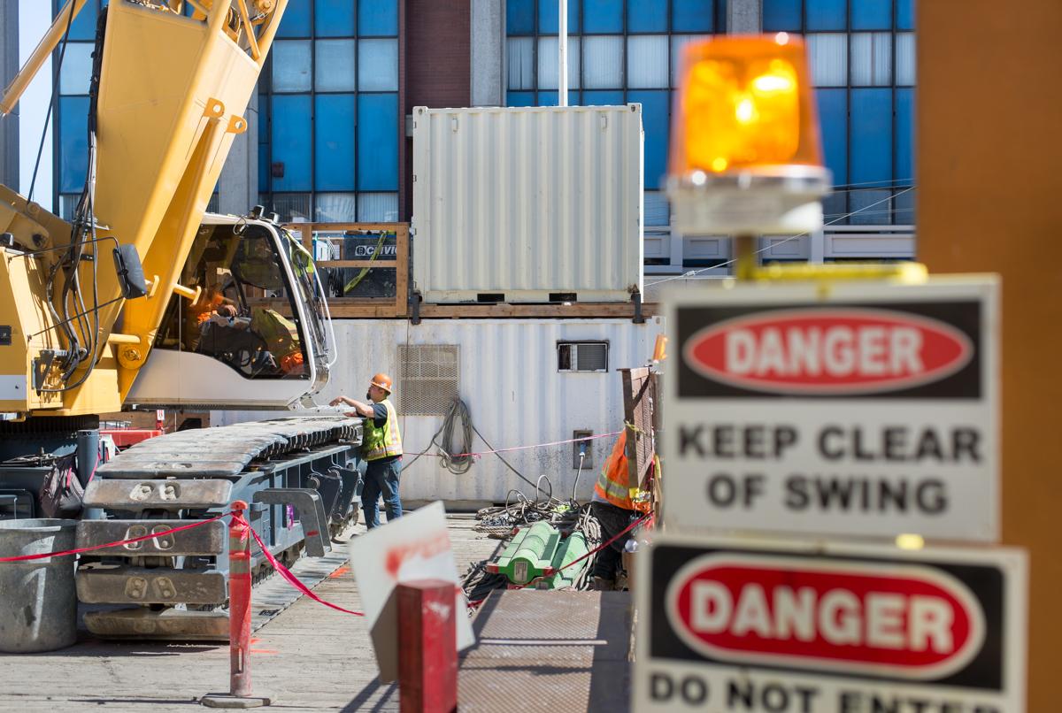 Construction site with crane, shipping containers, and danger signs at transit station.