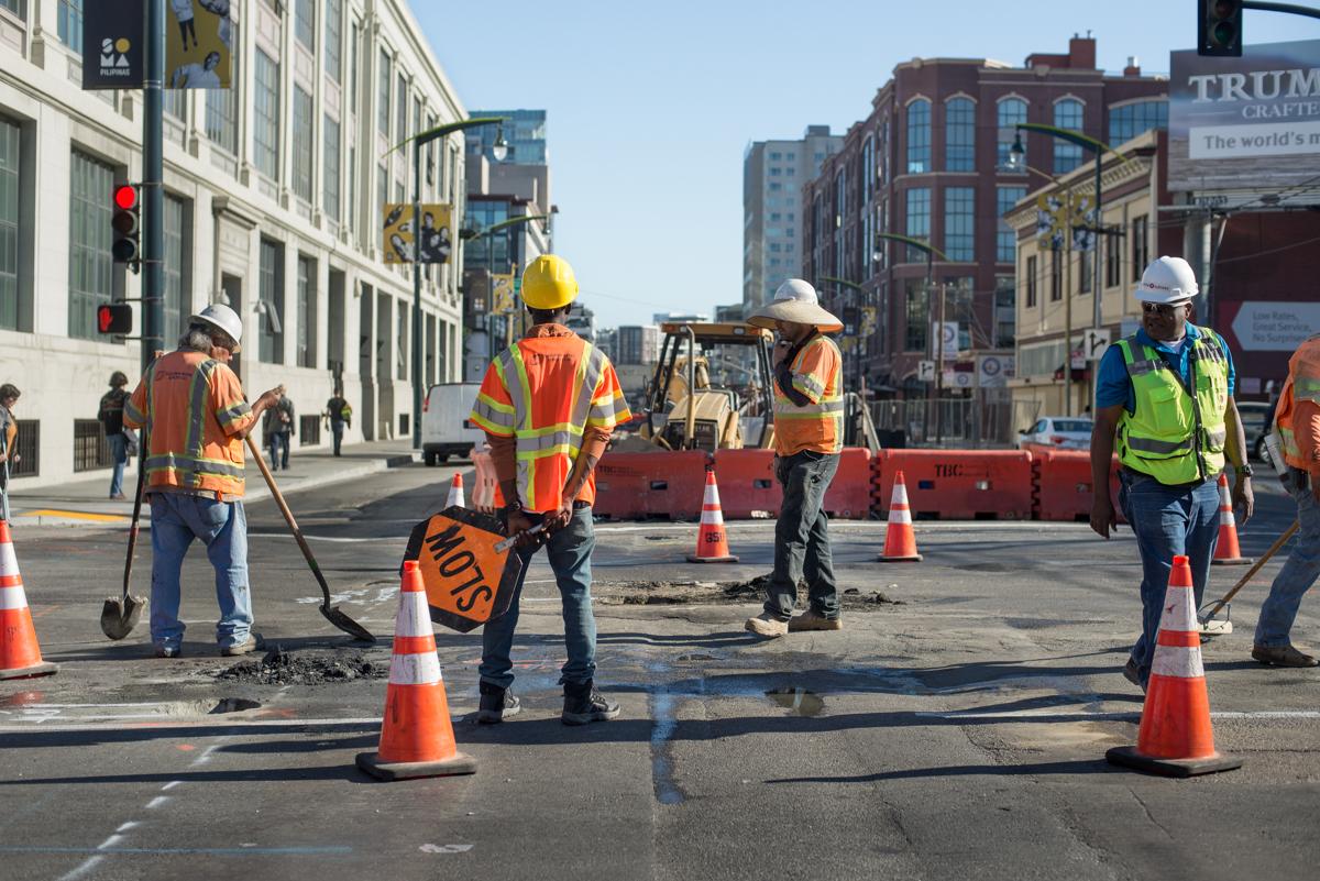 Construction crew performs utility potholing work on city street with traffic cones and safety equipment.