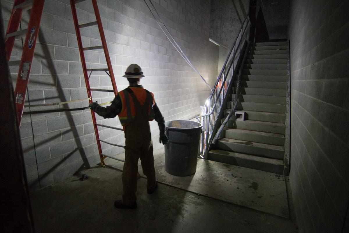 Worker in hard hat and safety vest holding ladder in underground station stairwell during construction.
