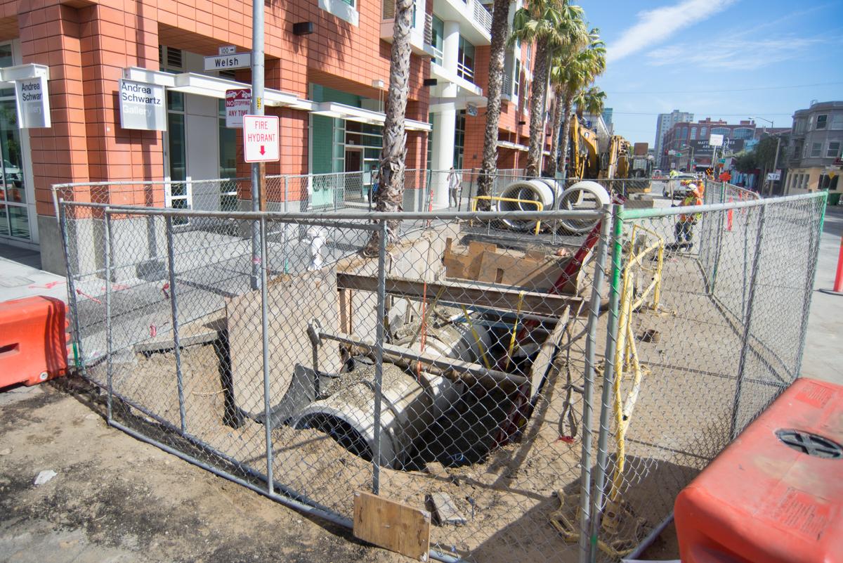 Construction site with fenced area containing equipment and workers installing underground sewer lines at 4th and Welsh.