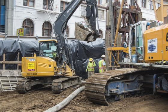 Excavation equipment and workers construct underground station walls for the future Chinatown Station.