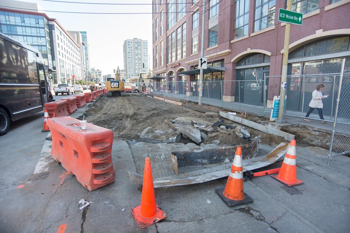 Construction site on 4th Street with excavation, orange barriers, and equipment blocking the roadway.