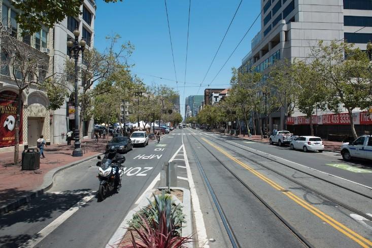 Motorcyclist riding westbound on Market Street with streetcar tracks and downtown buildings visible.
