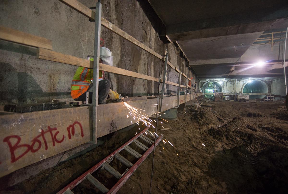 Worker using angle grinder on steel beam for temporary bracing inside underground transit station.