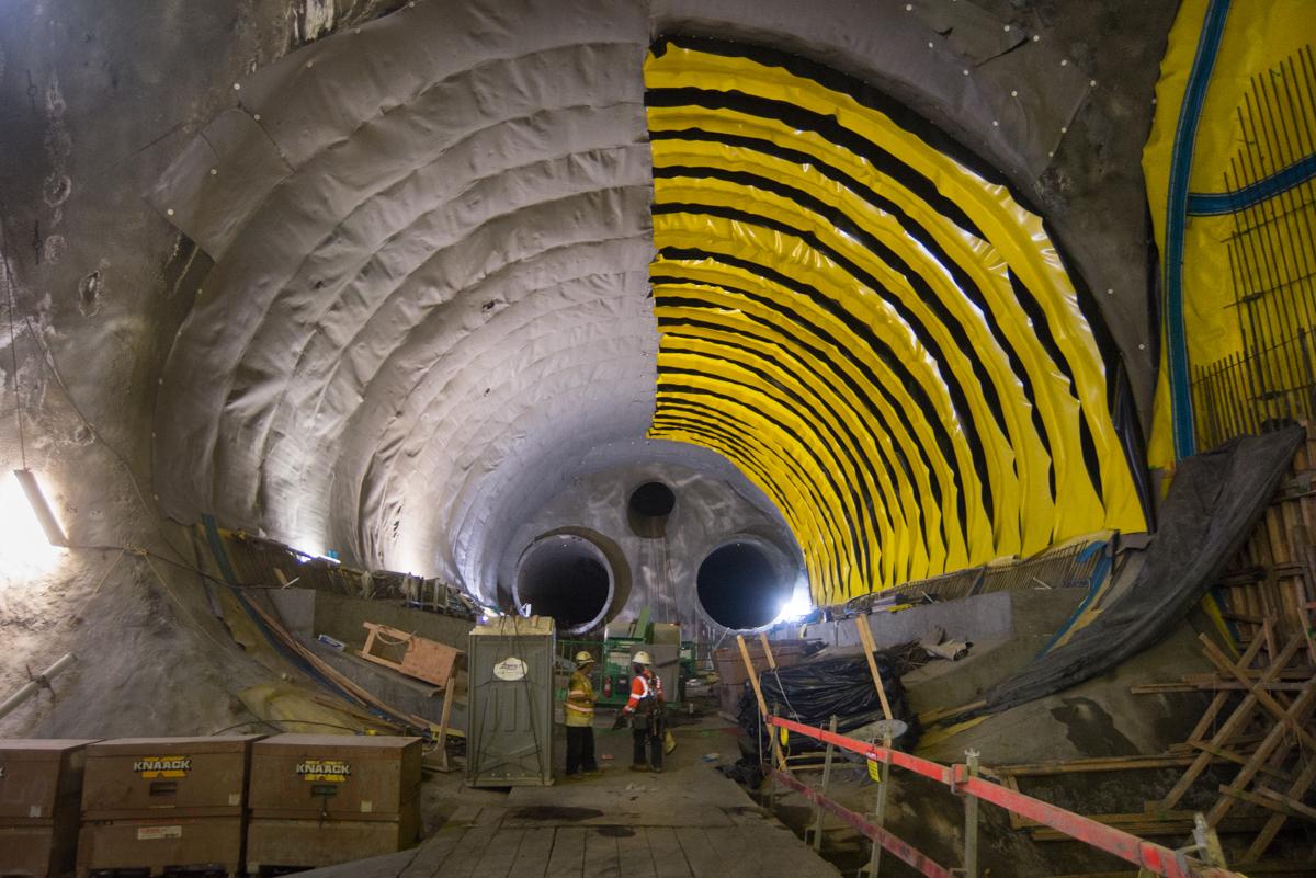 Underground tunnel under construction with yellow waterproofing sheets and workers installing materials on platform.
