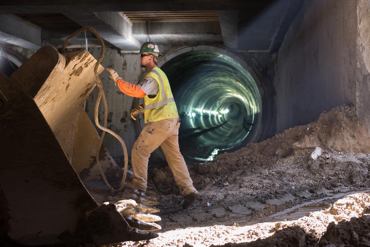 Worker in safety vest and hard hat positioning rope on excavation equipment inside tunnel under construction.
