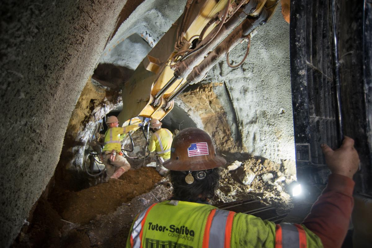 Workers in safety gear operate excavation equipment in underground tunnel during maintenance work.