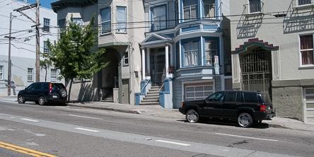 Street parking on Duboce Avenue with parked vehicles and Victorian buildings.