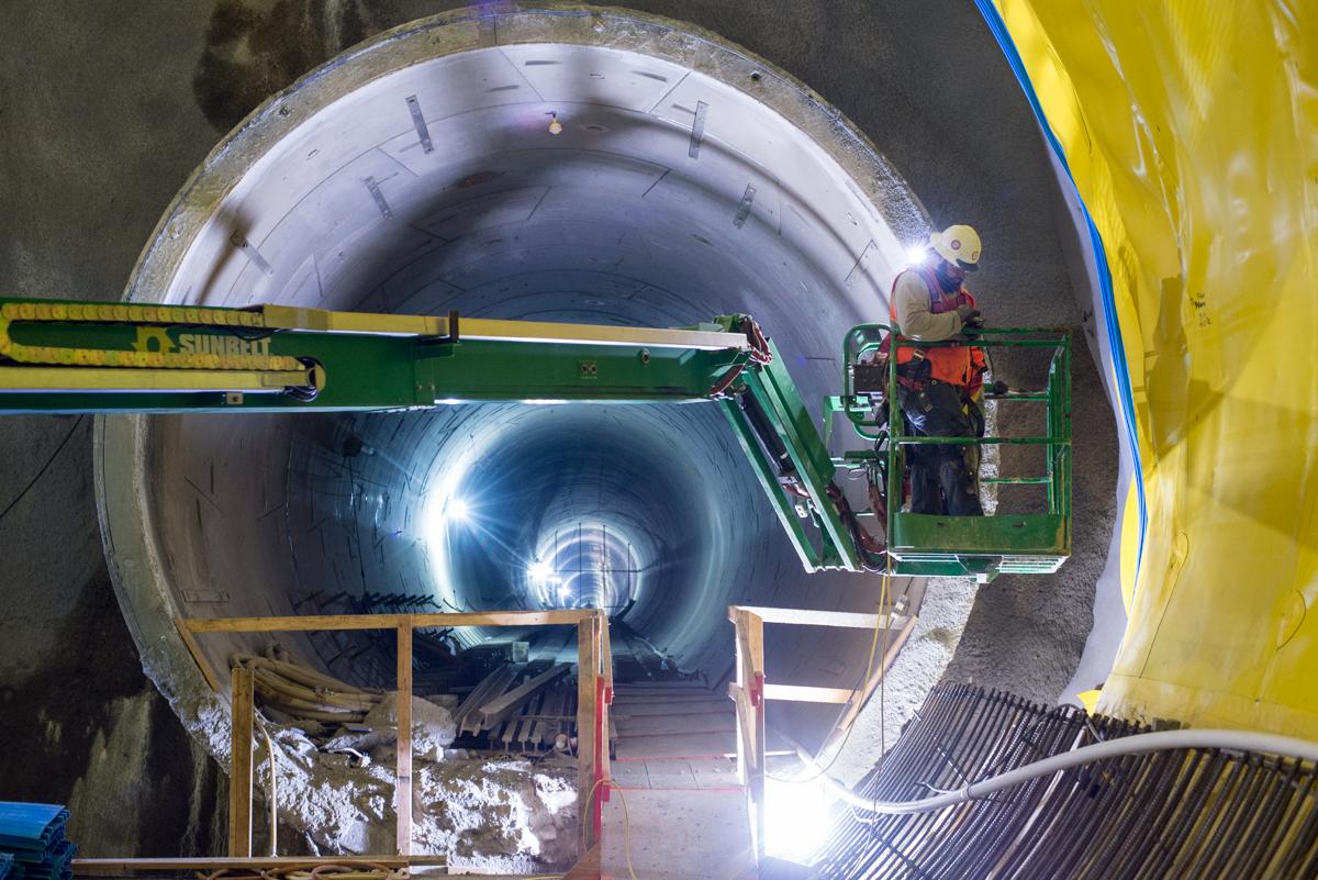 Worker in lift operates equipment inside tunnel during Chinatown Station platform construction.