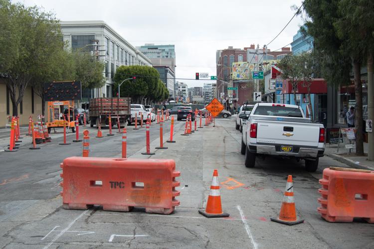 Construction site on 4th Street with orange barriers, traffic cones, and equipment for utilities relocation work.
