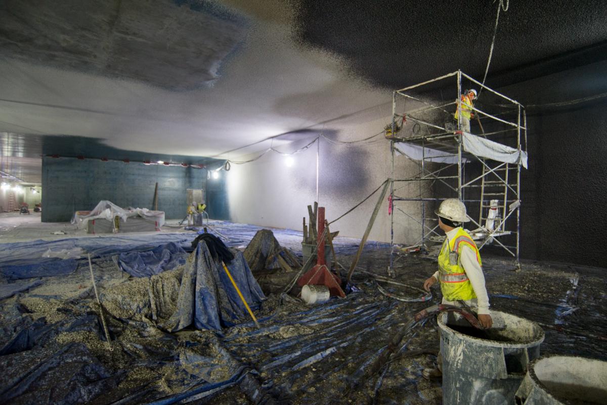 Construction worker smoothing concrete floor inside underground station box at night with scaffolding and equipment visible.