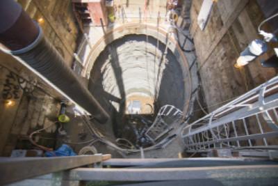 Workers and equipment at bottom of underground transit station headhouse shaft during construction.