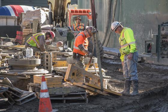 Construction workers in safety gear demobilizing equipment at a transit station excavation site.