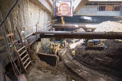 Construction site on Stockton Street with excavators and bulldozer removing soil beneath overhead structures.