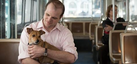 Man holding brown dog on streetcar with passengers in background