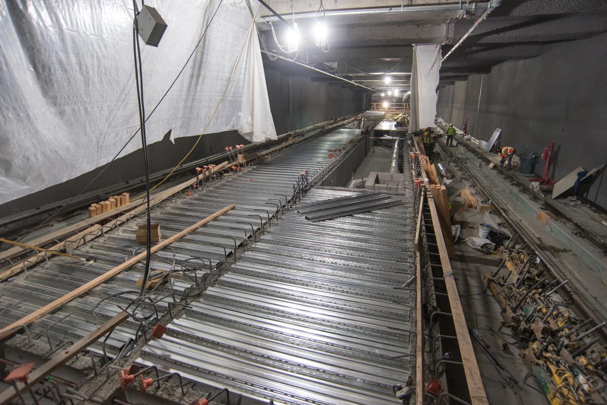 Construction of corrugated steel platform decking inside underground transit station box with exposed rebar and wooden formwork.