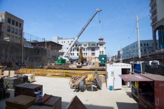 Construction site at Chinatown Station with crane, yellow barriers, and surrounding buildings under development.