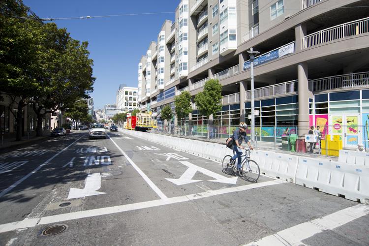 Cyclist riding on 4th Street at Harrison with white barriers, construction signage, and apartment buildings lining the street.