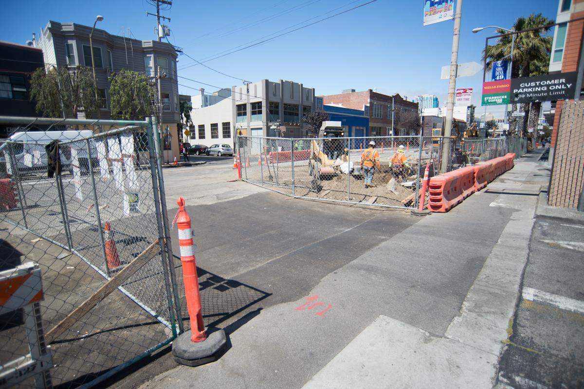 Construction site on 4th Street with fenced work area, traffic cones, and workers installing underground utilities.