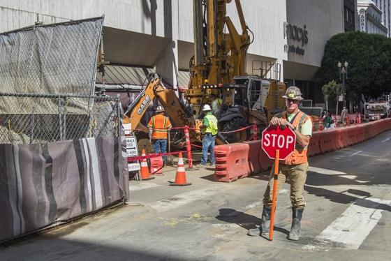Construction crew with stop sign and equipment on city street during sewer line work.