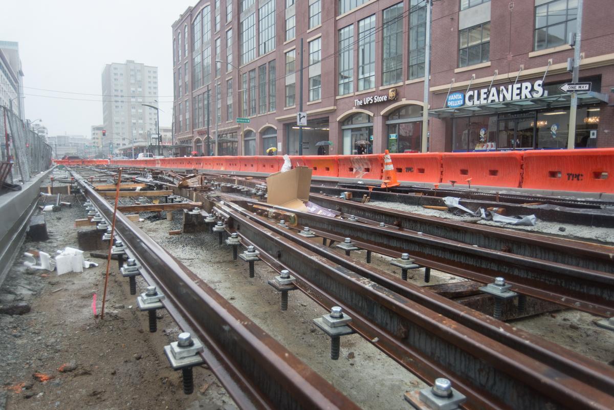Railroad tracks under construction in urban tunnel with red equipment and brick buildings.