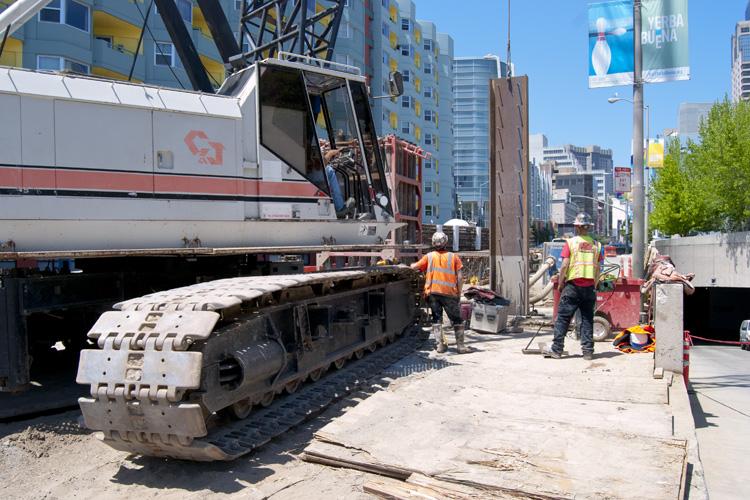 Construction equipment and workers at 4th and Folsom Street site with excavator and delivery truck.