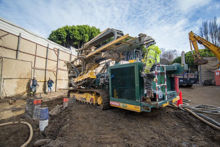 Construction site with yellow drilling equipment, green generator box, and workers in safety vests near Stockton Street tunnel project.