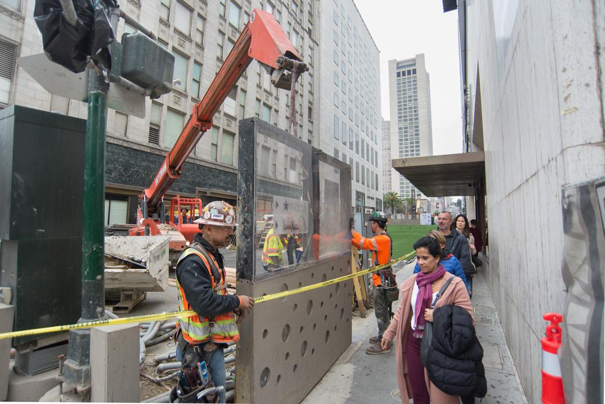 Construction crew installing pedestrian safety barrier on urban street with high-rise buildings.