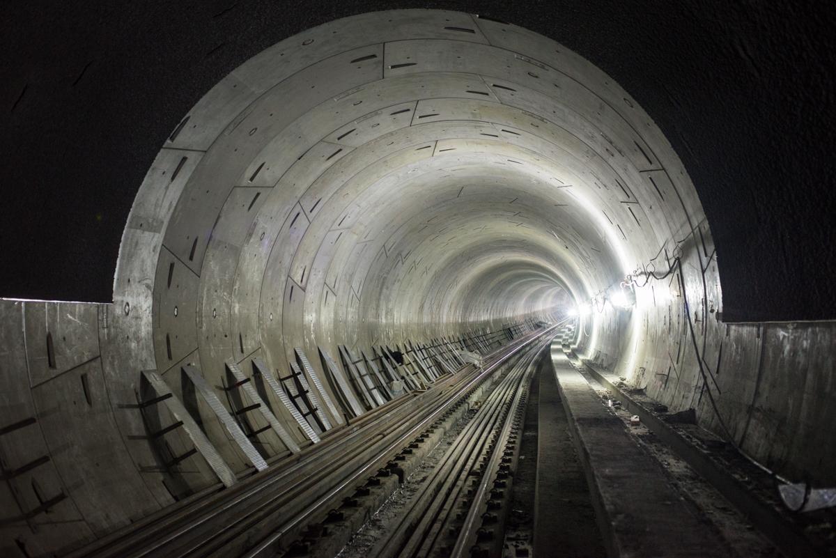 Interior of subway tunnel with steel reinforcement ribs, railroad tracks, and lighting extending toward station ahead.