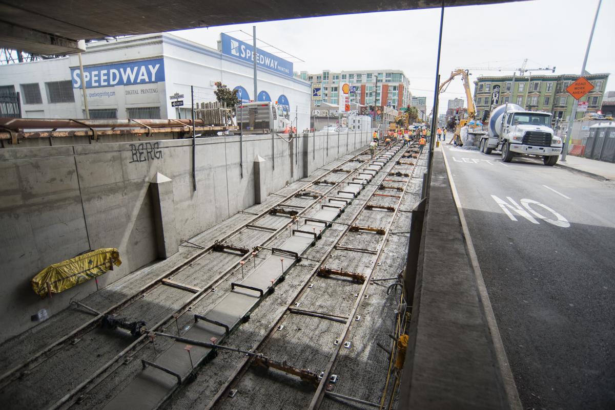 Central Subway tunnel construction site with concrete tunnel sections and railway tracks under the Speedway overpass.