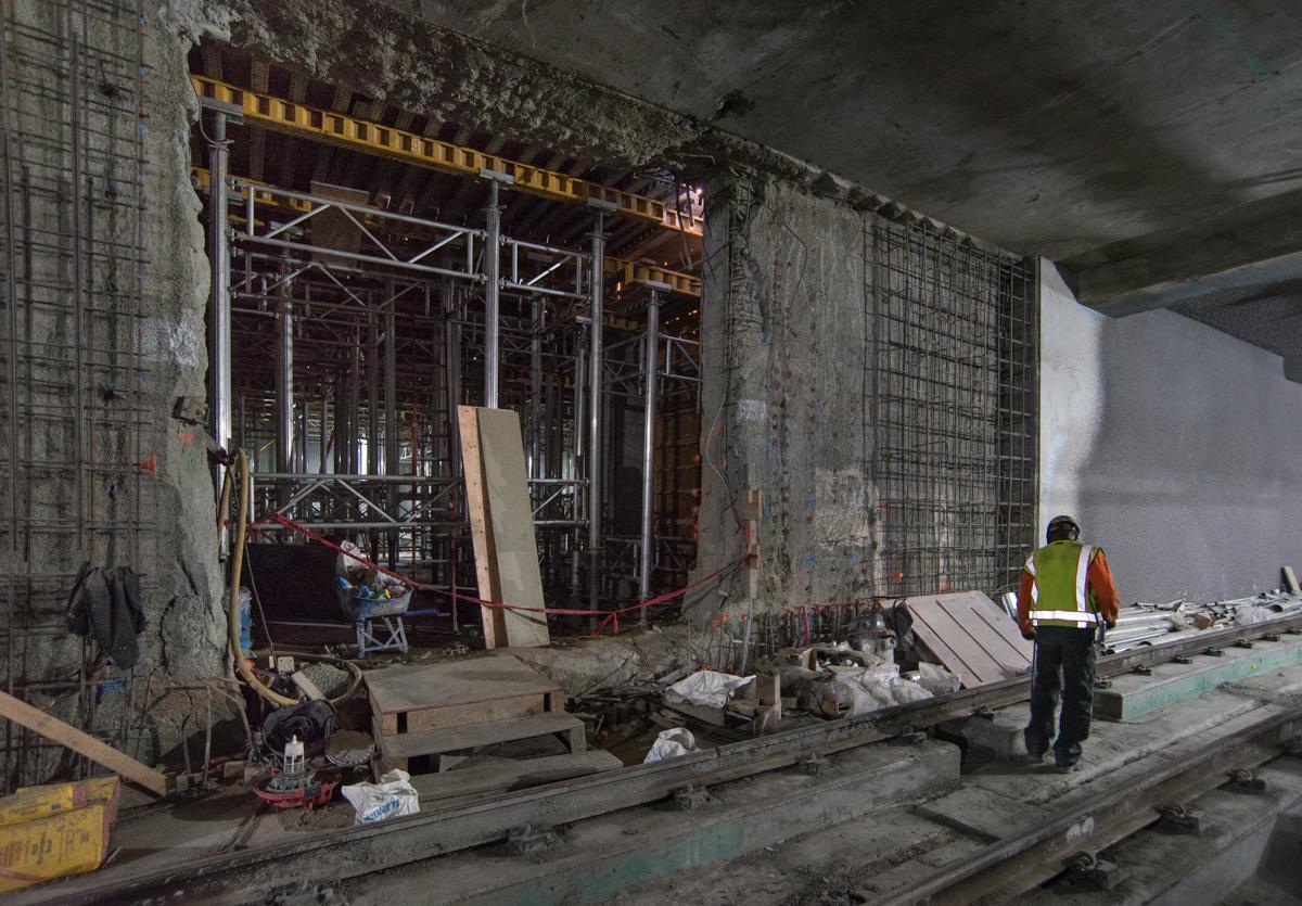 Construction worker in safety vest walks past concrete formwork and steel scaffolding at Yerba Buena/Moscone Station platform.