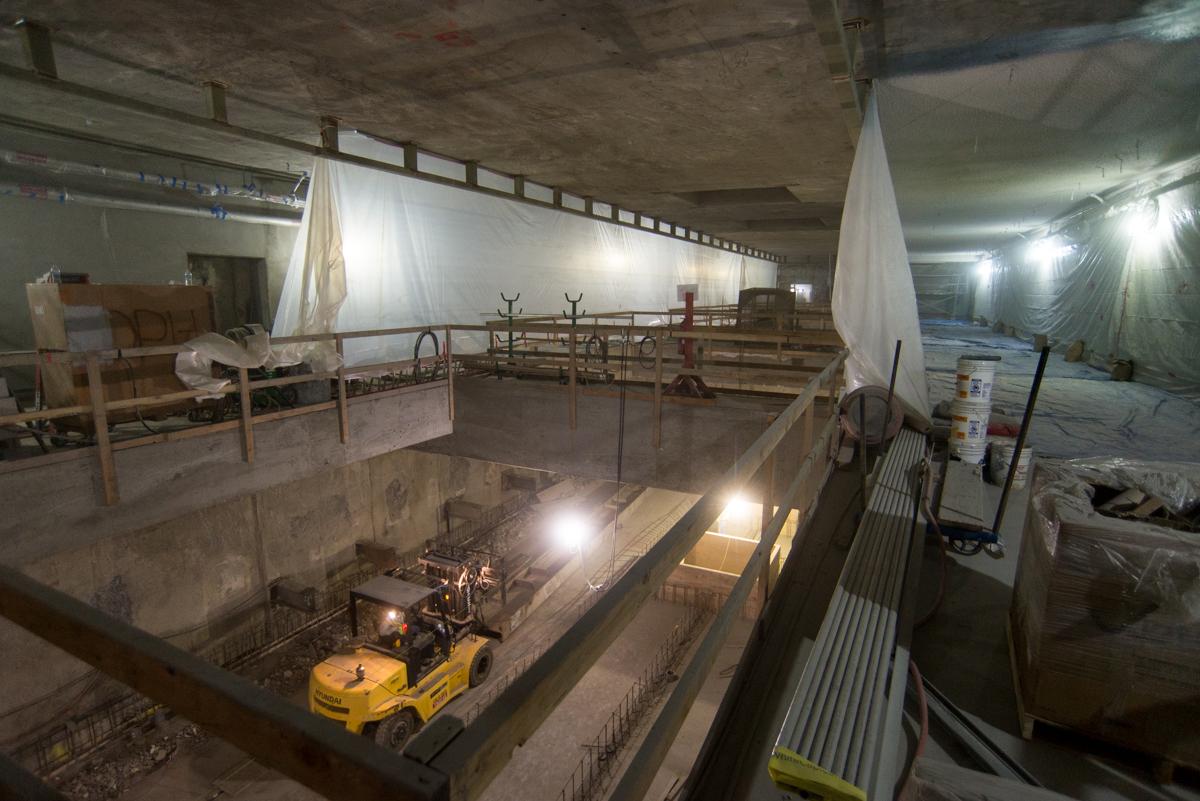 Construction work inside underground transit station with yellow equipment and plastic containment sheeting.
