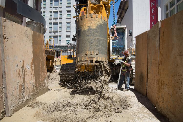 Construction site on Folsom Street showing excavated material, equipment, and plywood barriers containing the work area.