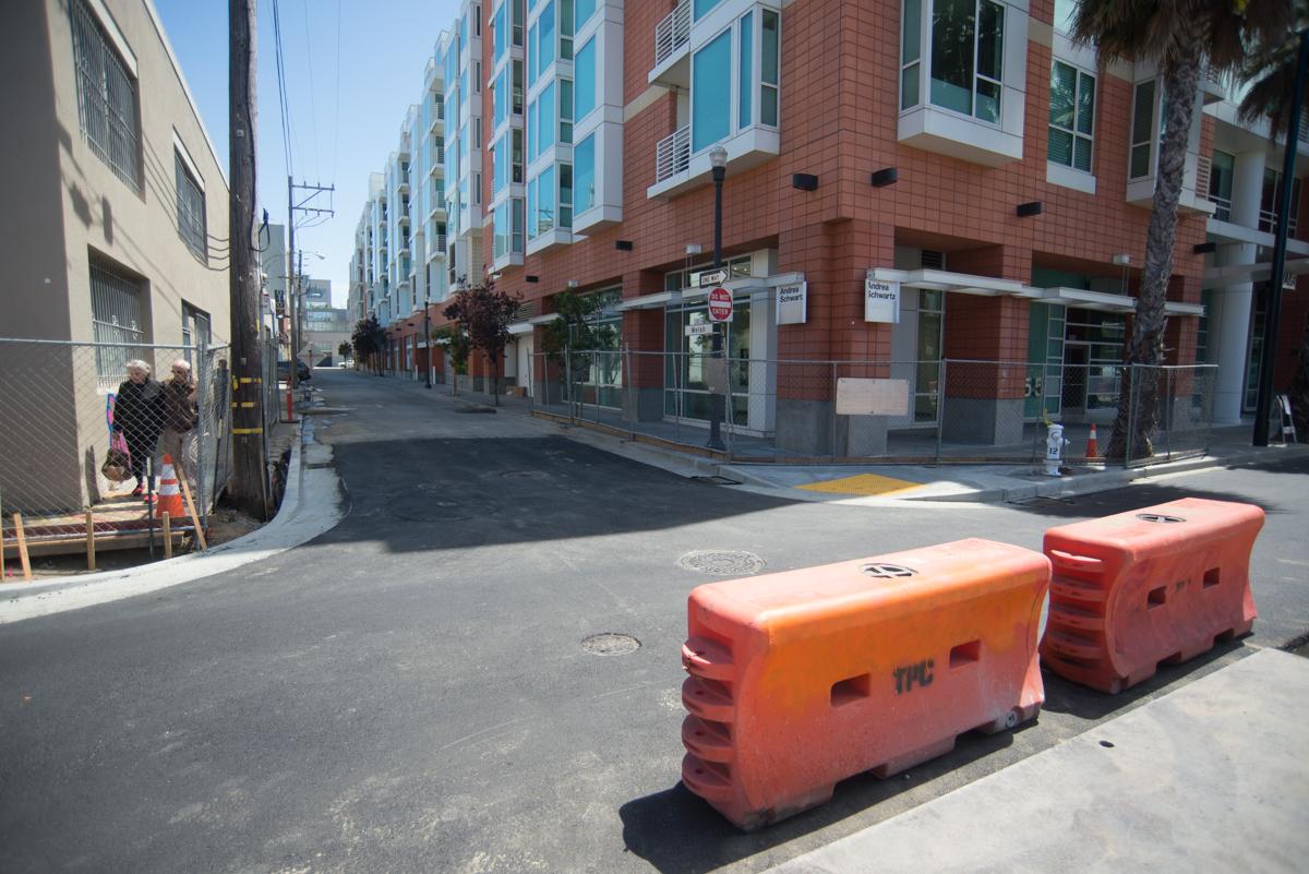 Orange and red plastic barriers block a street lined with brick apartment buildings and storefronts.