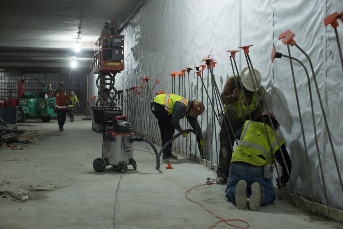 Construction workers in safety vests install wall anchors inside Yerba Buena Moscone Station.