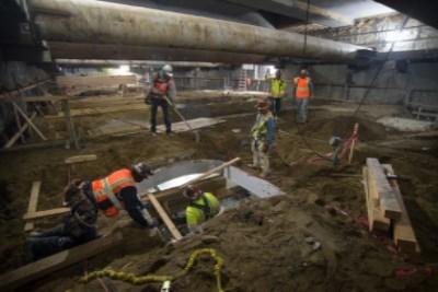 Workers in safety vests excavate underground station box on Folsom Street at night.
