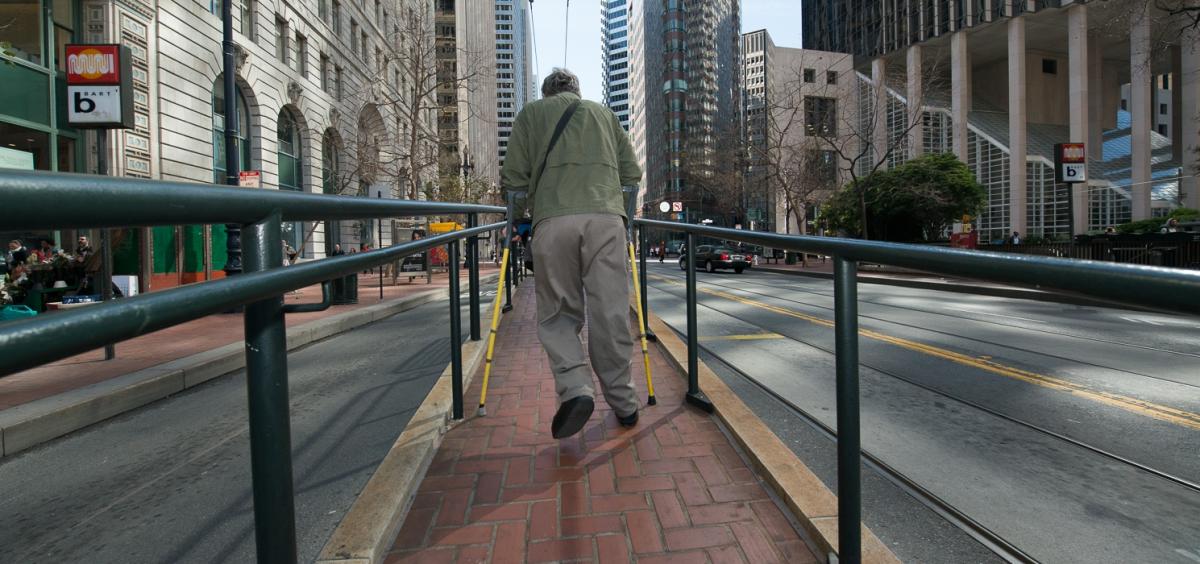 Person using mobility aid on streetcar boarding ramp with yellow tactile warning strip on Market Street