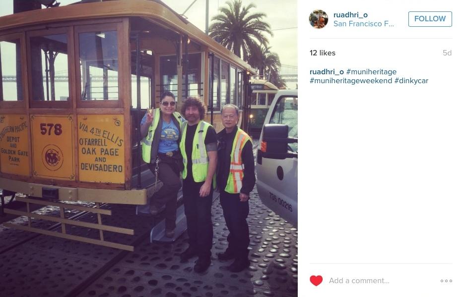 Four people posing next to cable car 578 on San Francisco street with palm trees in background