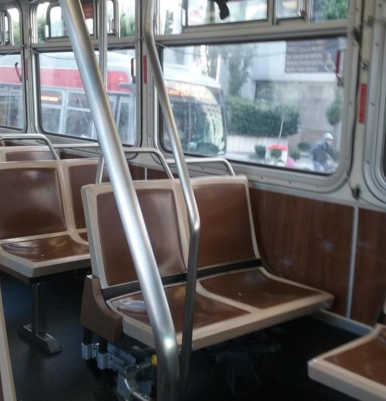Interior of transit bus with brown seats, metal handrails, and windows showing street view outside.