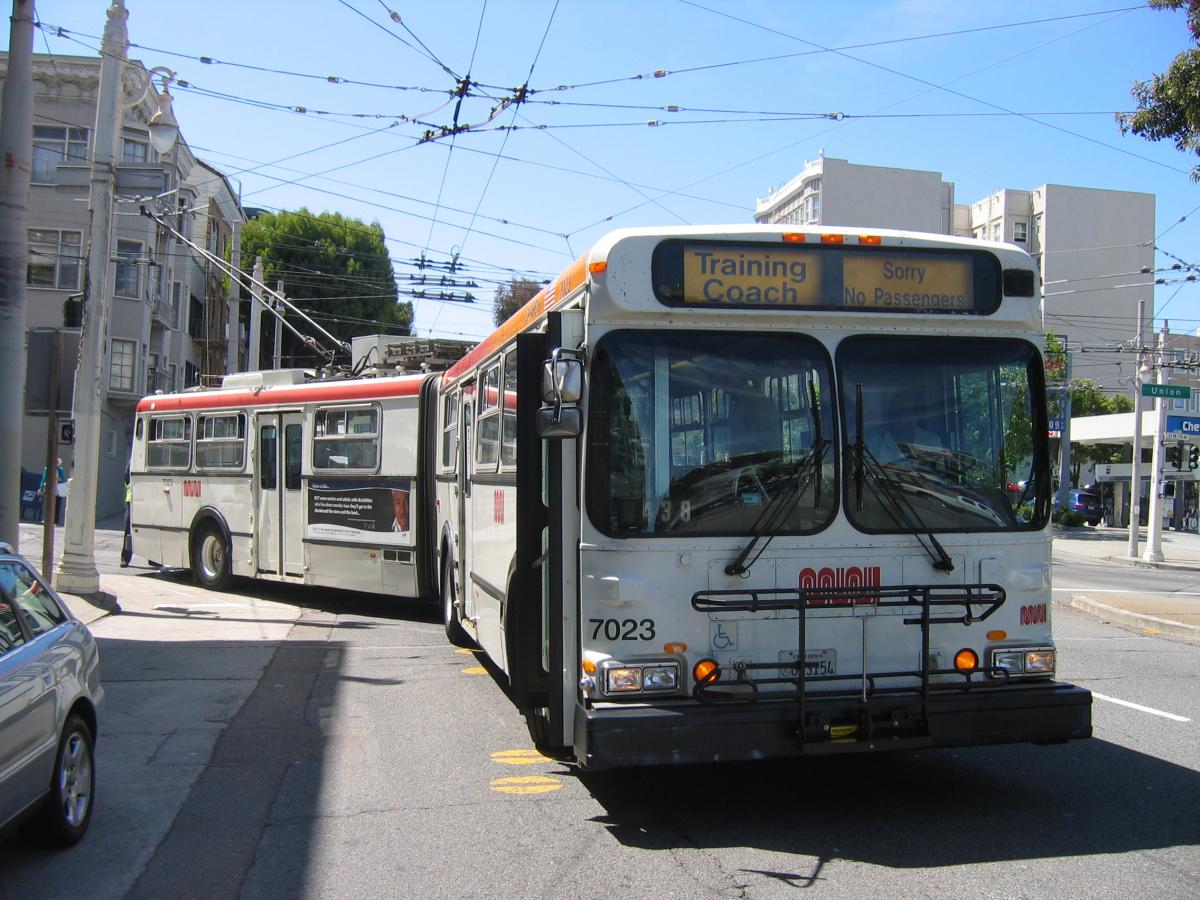 Muni training coach 7023 with instructor and trainee operator on San Francisco street.